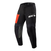 Black motorcycle pants with gray protective panels, a bright orange accent patch on the upper left leg, and a white 'REV'IT!' logo on the upper right thigh, shown against a plain white background.