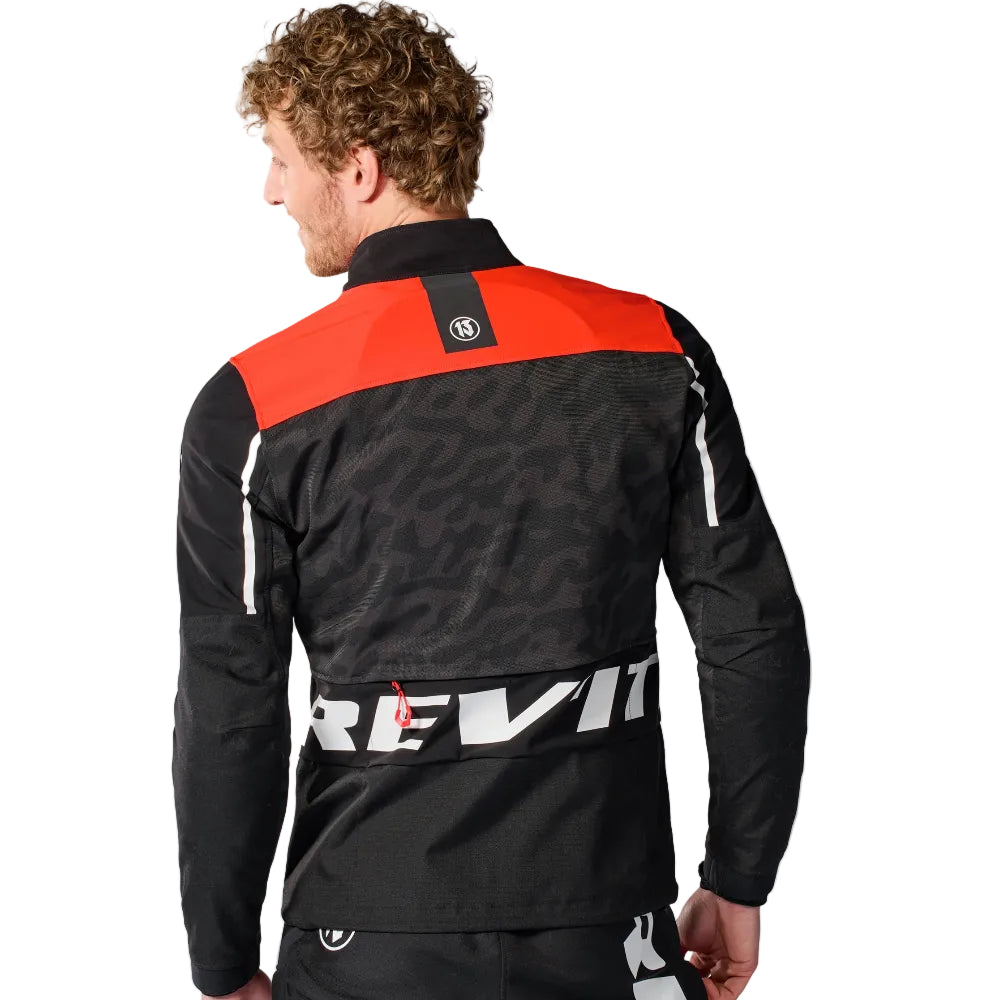 Person wearing a black and red jacket with 'Rev'it!' logo on a white background