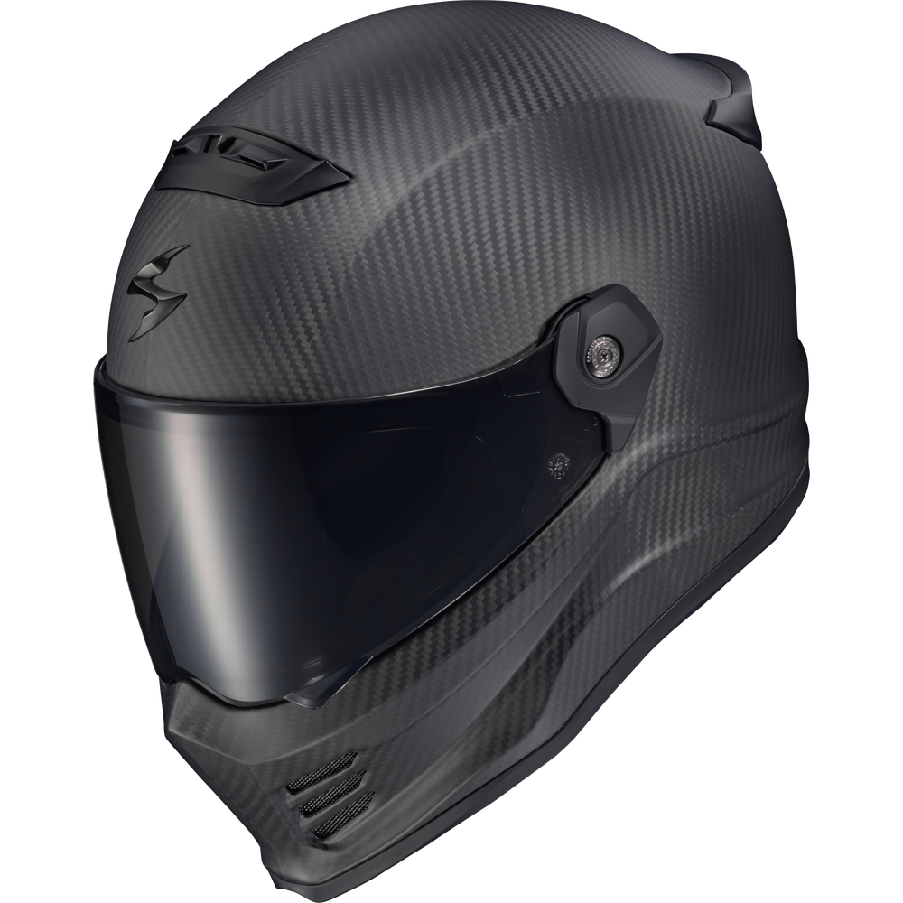 A full-face motorcycle helmet in a matte black carbon fiber pattern, featuring a dark tinted visor and a stylized logo on the side, shown against a plain white background.