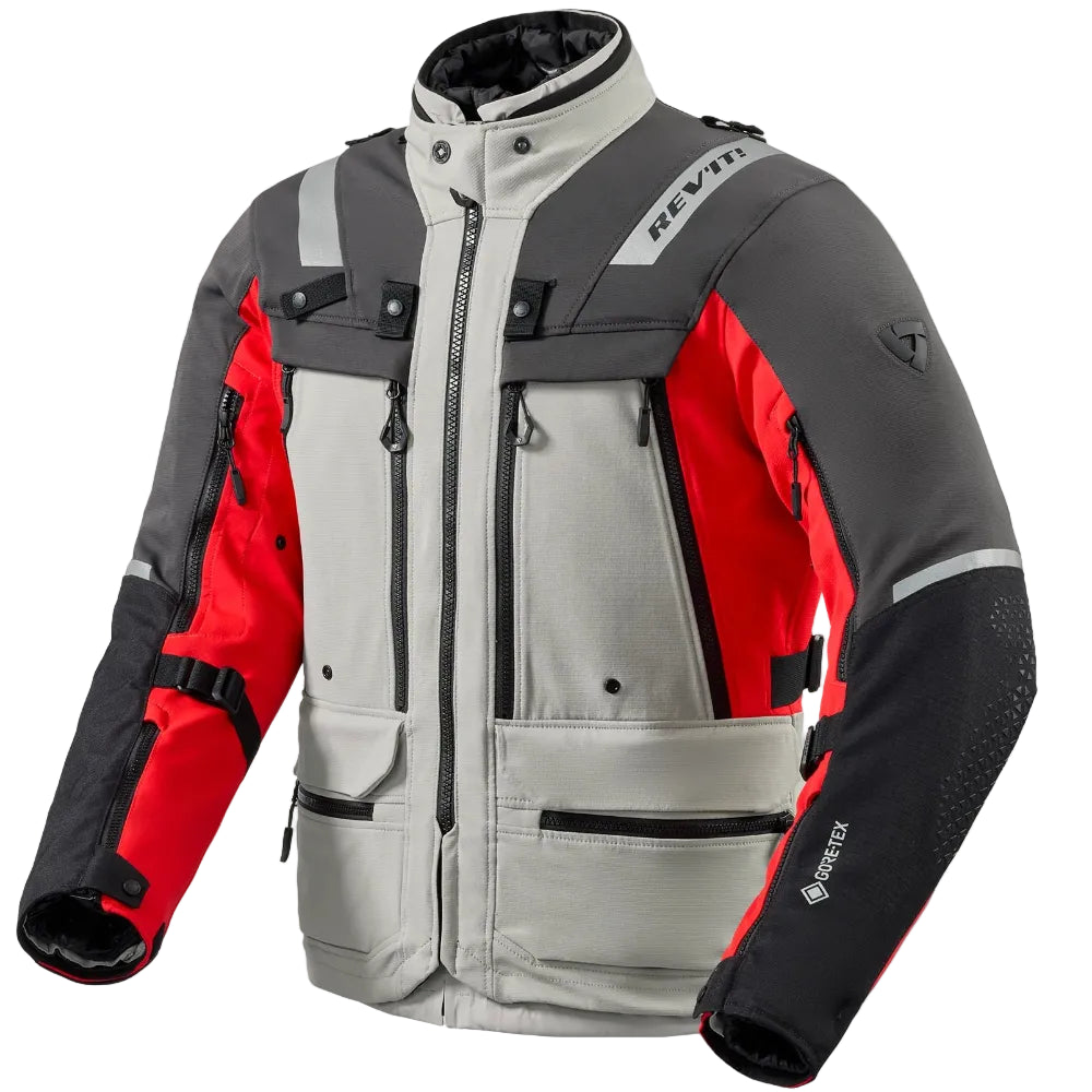 A technical motorcycle jacket in gray, black, and red, shown on a light beige background. The jacket features a high collar, multiple zippered pockets, and reflective details.