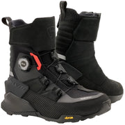 A pair of black mid-calf riding boots with a dial closure system and a small red accent, displayed on a light beige background. The brand 'Vibram' is visible on the toe area.