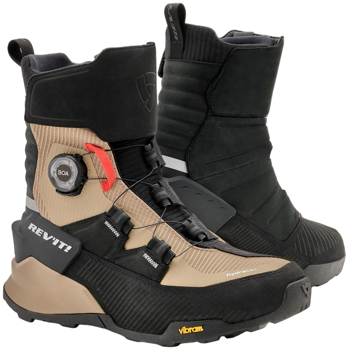 A pair of REV'IT! mid-calf riding boots in black and tan, featuring a dial closure system and a textured sole, shown against a light off-white background.