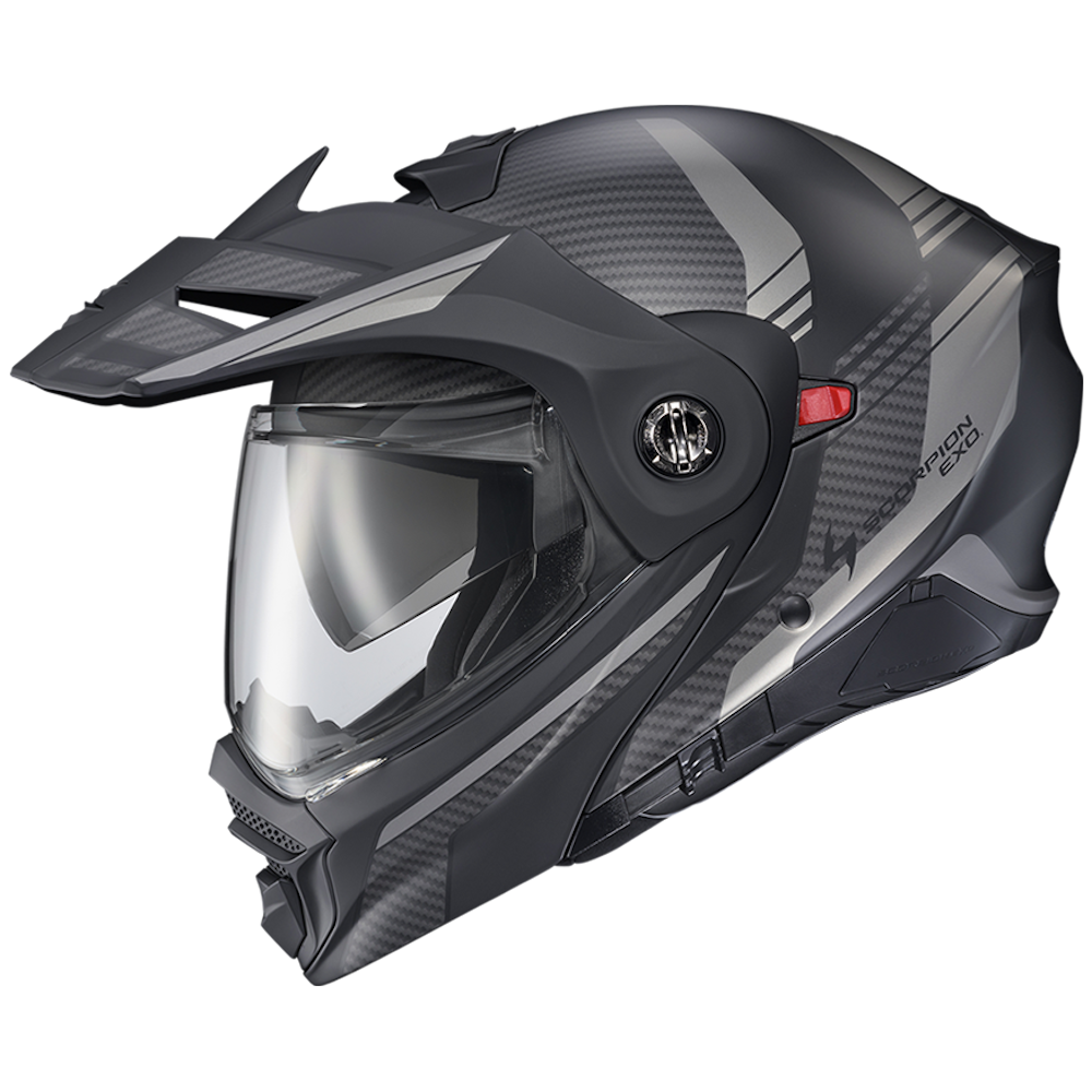 A full-face off-road motorcycle helmet in matte black and dark gray with a carbon fiber pattern, featuring a clear visor and a small red switch.