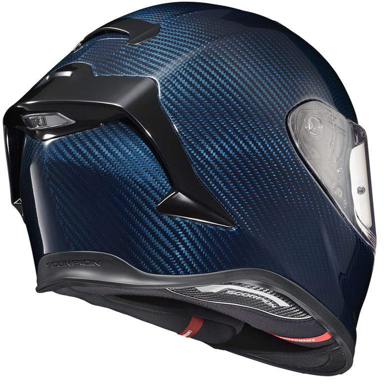 A full-face motorcycle helmet featuring a glossy dark blue carbon fiber pattern with black structural accents and a clear visor, shown from a three-quarters rear angle on a white background.