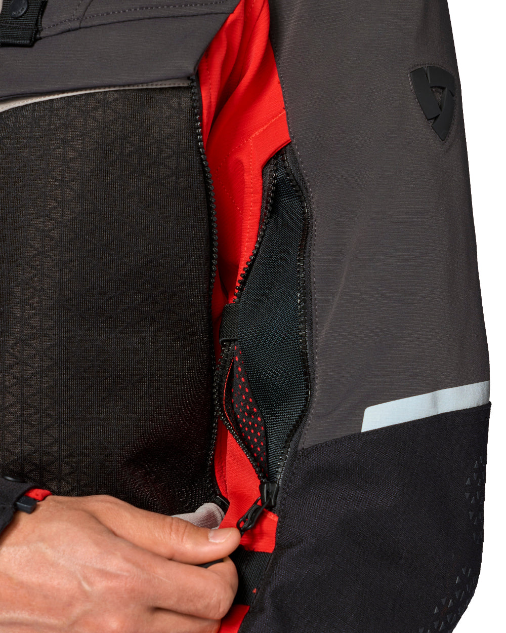 Close-up of a dark gray and black technical jacket with a red interior lining, showing a hand opening a zippered pocket.