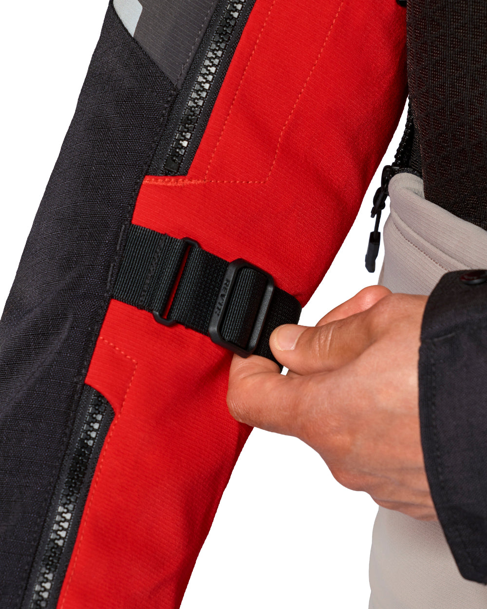 Close-up of a person's hand fastening a black plastic buckle strap onto a red and black insulated jacket sleeve, with a white background.
