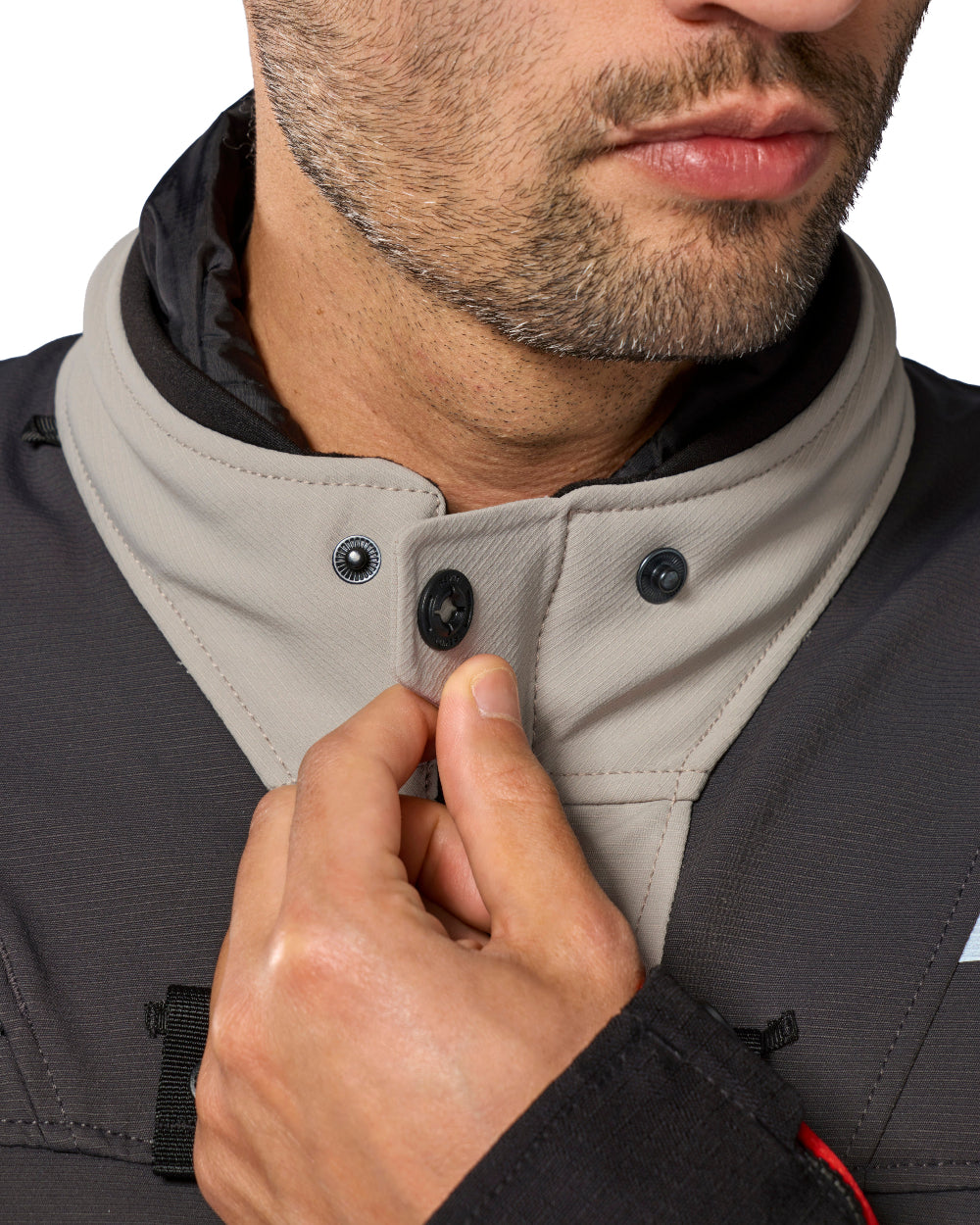 Close-up of a man wearing a light beige high collar with black snap buttons over a dark gray jacket, adjusting the collar with his hand.