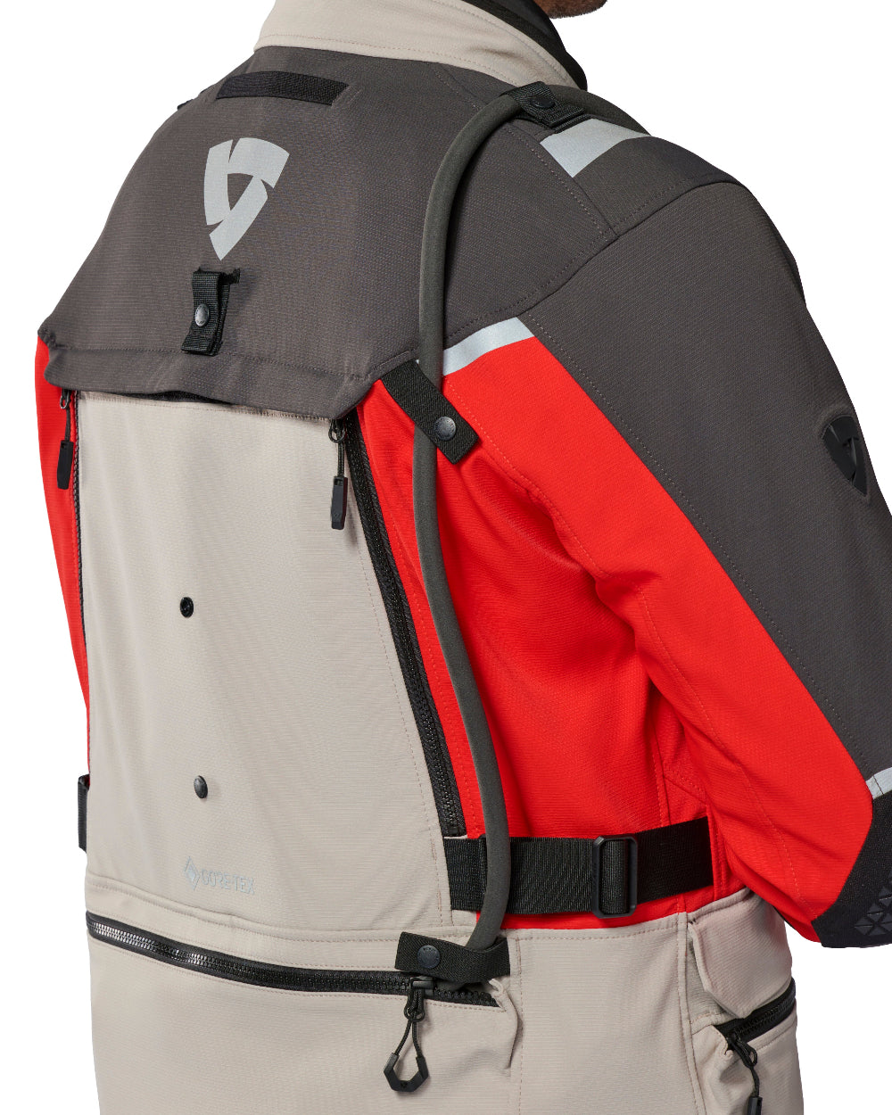 Close-up rear view of a technical outdoor jacket with a gray shoulder panel, red sleeves, and light beige body sections, shown on a person against a white studio background.
