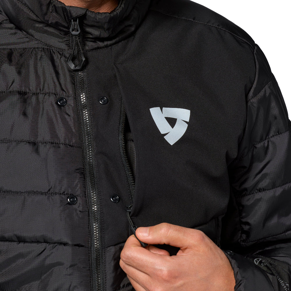 Close-up of a black puffer jacket worn by a model, featuring a silver geometric shield logo on the left chest and a front zipper.
