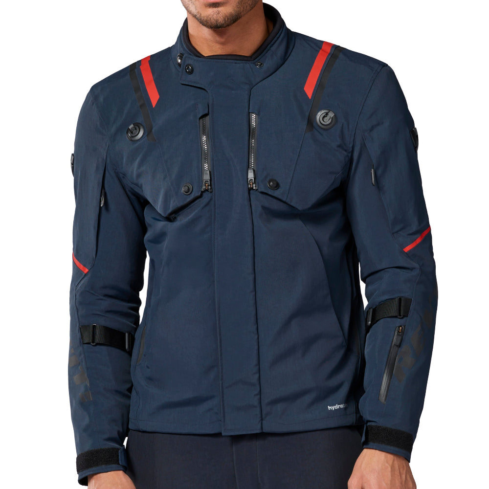 A man wearing a dark navy blue technical jacket with red accents and matching dark pants, photographed against a plain white background.