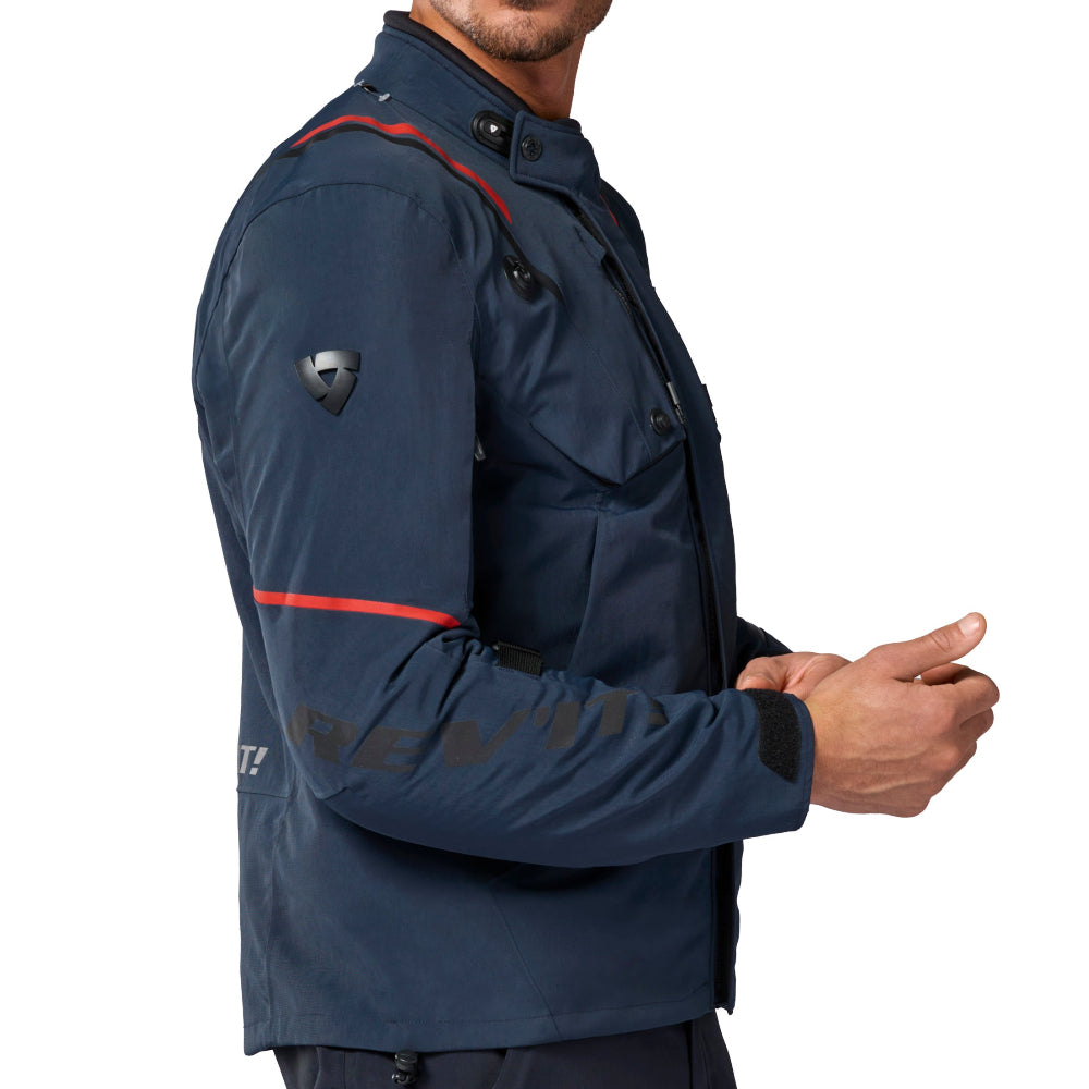 A man wearing a navy blue technical jacket with red reflective striping and matching dark pants, photographed against a plain white background.