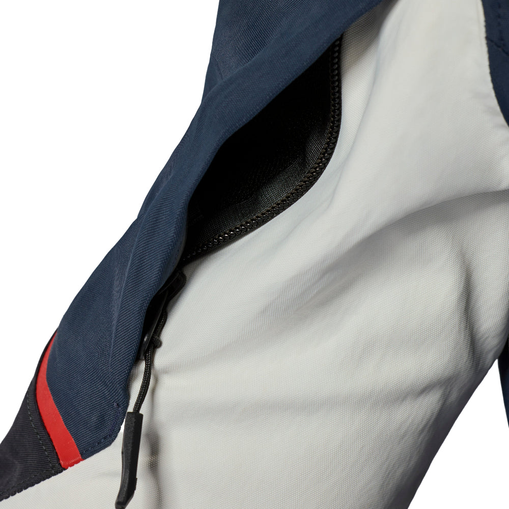 Close-up of a technical jacket showing a white outer shell, a navy blue sleeve or upper section, a black zipper, and a red accent stripe on a white background.