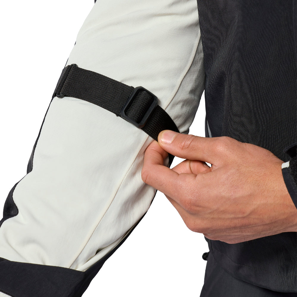 Close-up of a person wearing a light gray and black sleeveless jacket or suit, fastening a black elastic strap around the upper arm with their hand against a white background.