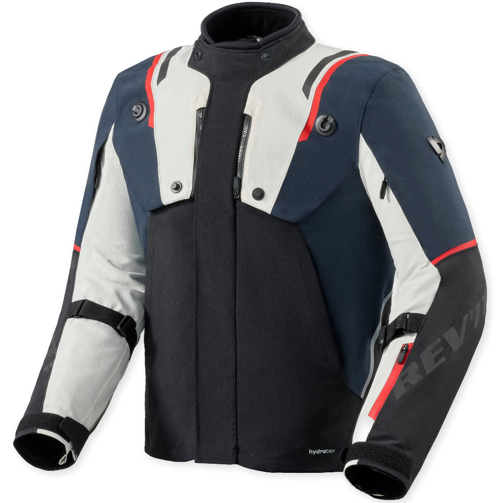 A technical motorcycle jacket in navy blue, white, and black with red accents, featuring a high collar, front zipper, and visible 'Revit' branding on the sleeve.