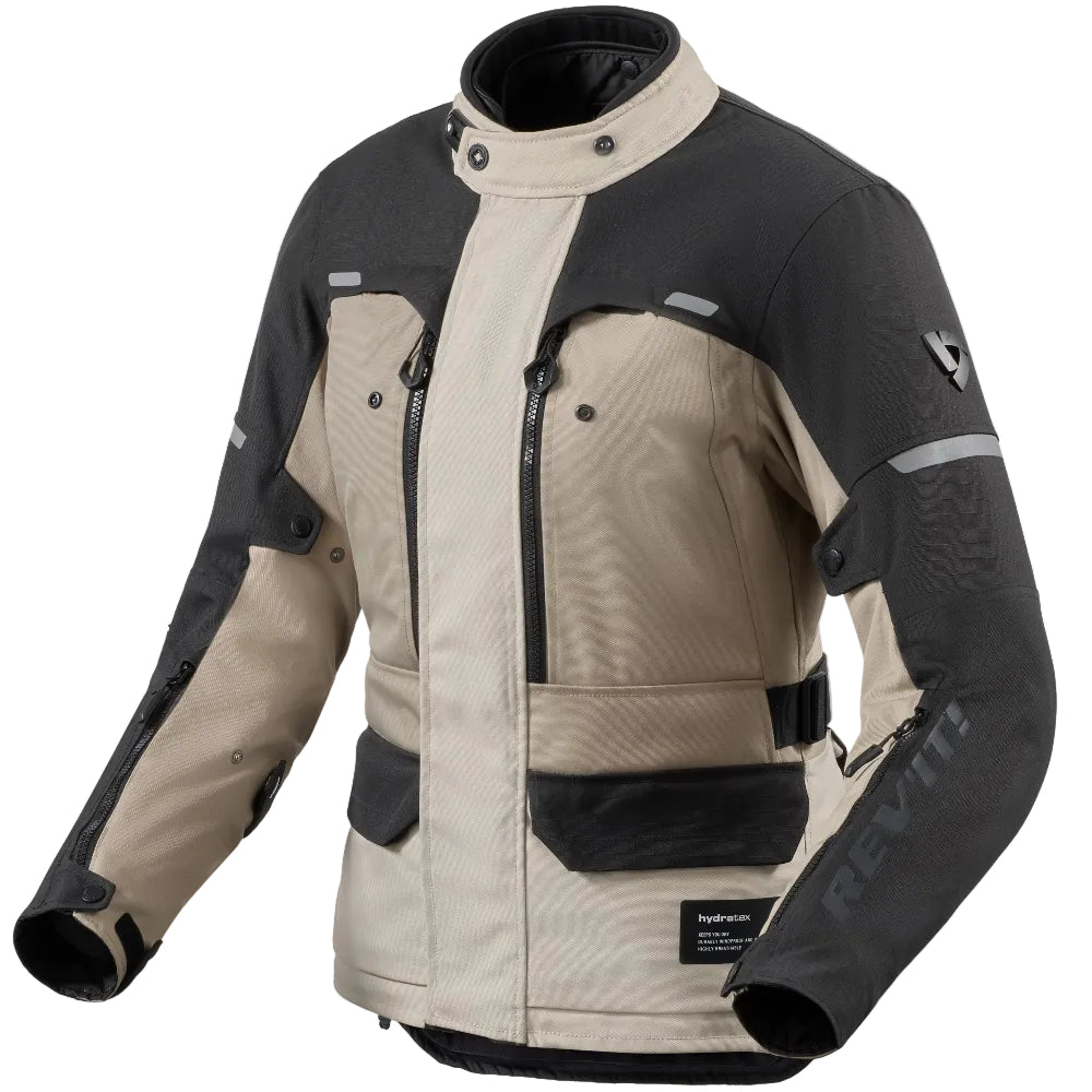A beige and black REV'IT! motorcycle jacket with multiple zippered pockets and reflective details, shown on a plain white background.