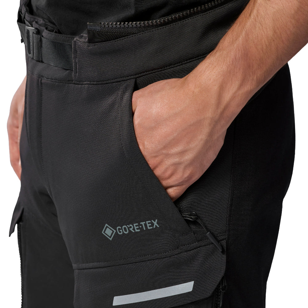 Close-up of a person wearing black technical pants with a hand in the side pocket, showing a GORE-TEX logo and a reflective strip on the leg.