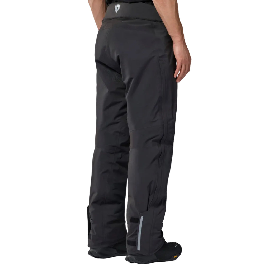 Rear view of a person wearing dark gray technical pants with a small white logo on the waistband, shown against a plain white background.