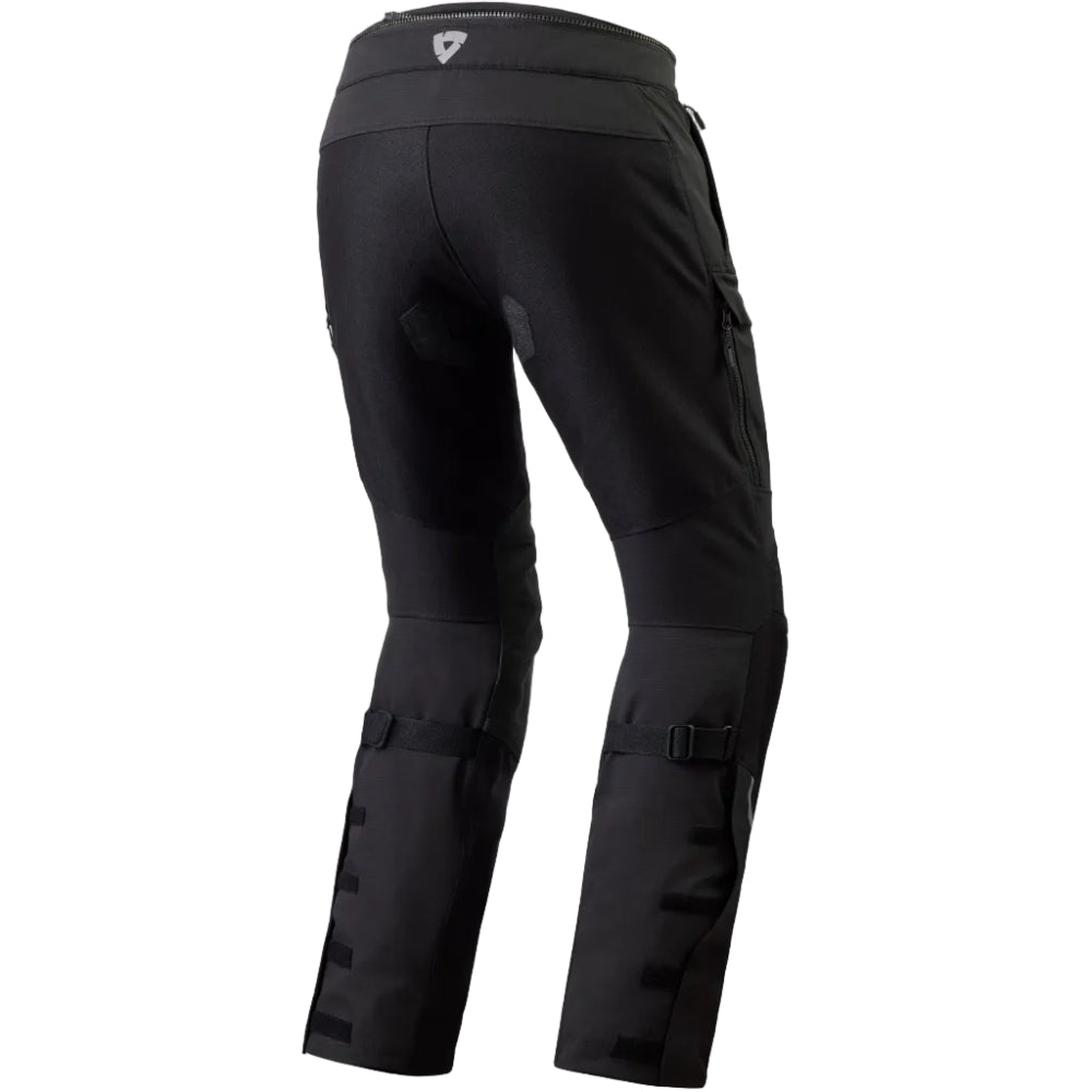 Black technical riding pants shown from the rear, featuring a high waistband with a small white logo, side cargo pockets, and lower leg buckle straps, photographed on a white background.