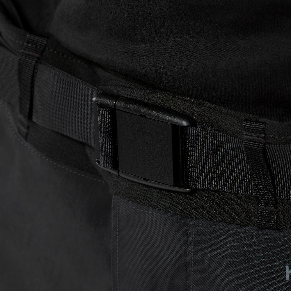 Close-up of a black belt with a matte black buckle attached to dark cargo-style pants.