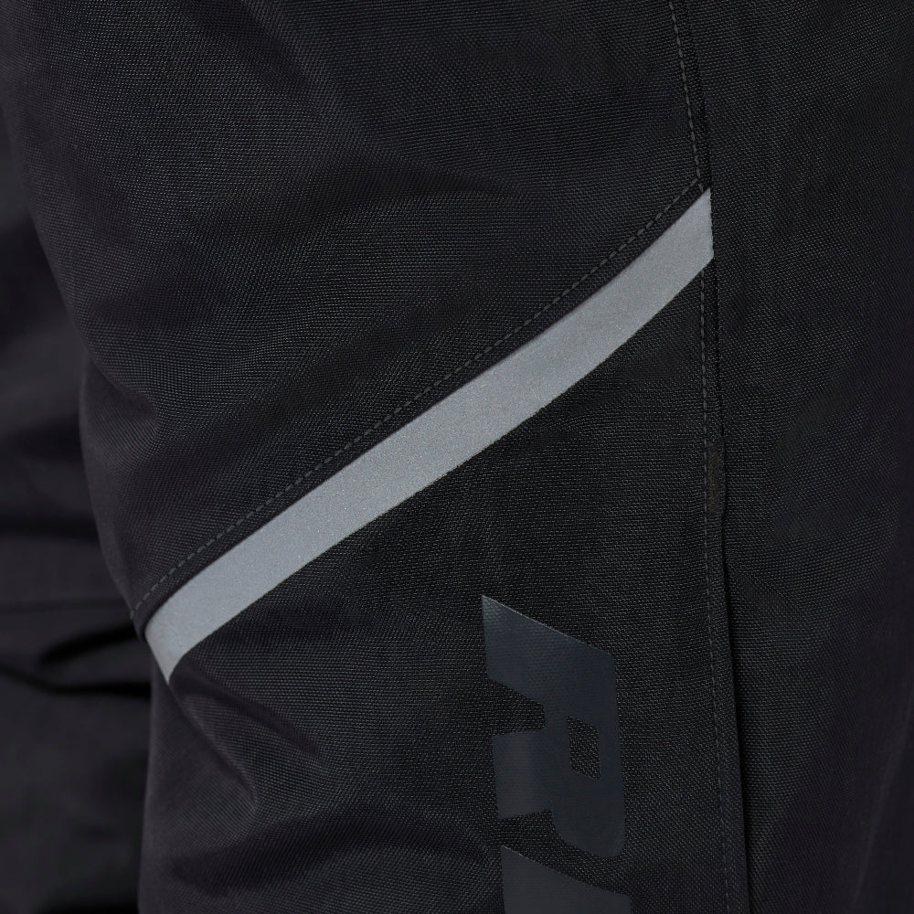 Close-up of black technical apparel, likely a jacket or pants, featuring a diagonal reflective gray stripe and a large tonal gray 'RE' logo on the lower leg.
