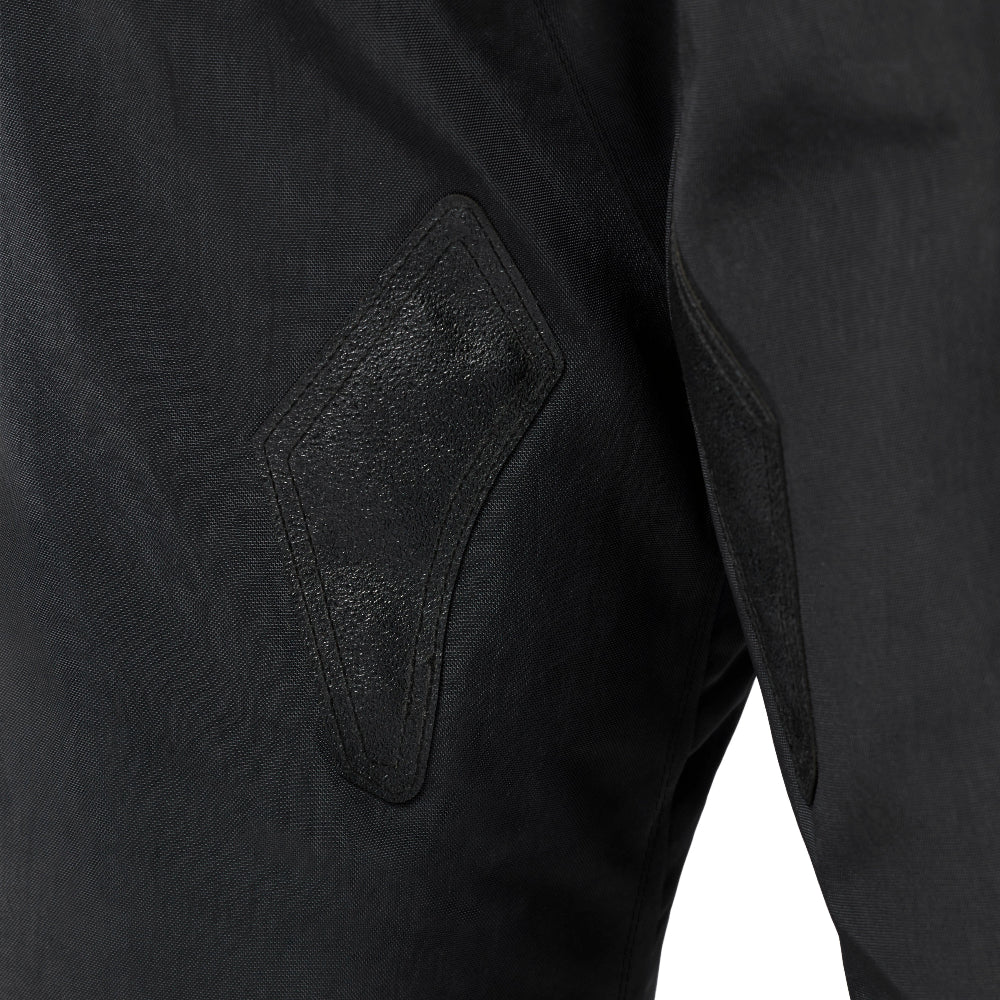 Close-up of black pants showing a diamond-shaped patch pocket with tonal stitching and textured paneling.