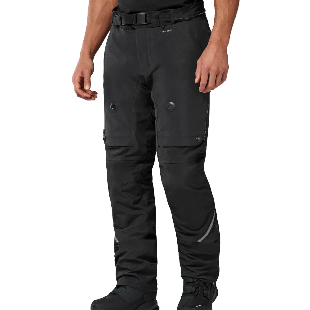 A person wearing black technical outdoor pants with a matching black belt, shown from the waist down on a light gray studio background.