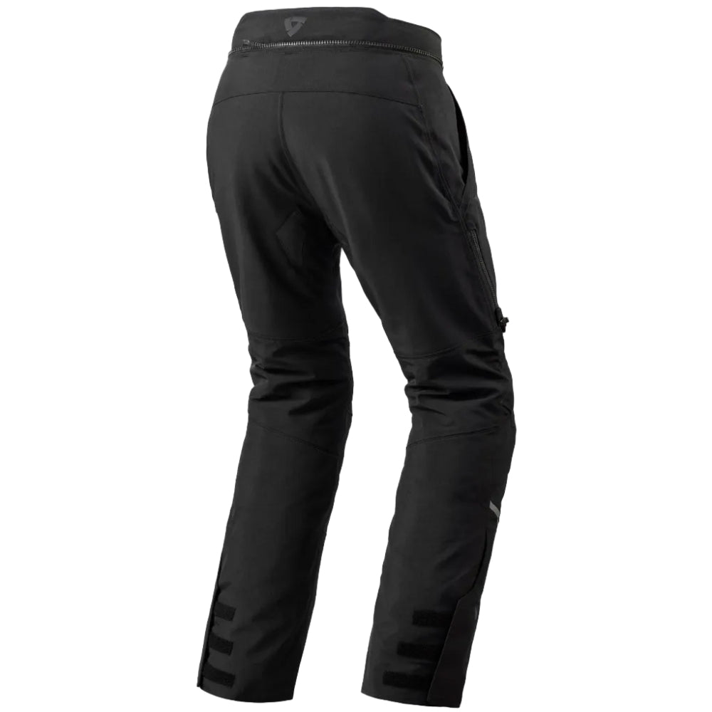 Black technical riding pants shown from the rear, featuring a high waistband with a small white logo, side cargo pockets, and lower leg buckle straps, photographed on a white background.