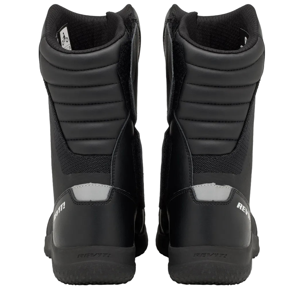A pair of black high-top motorcycle boots shown from the rear, featuring protective armor plates and a small silver reflective strip on the heel, set against a plain light gray background.