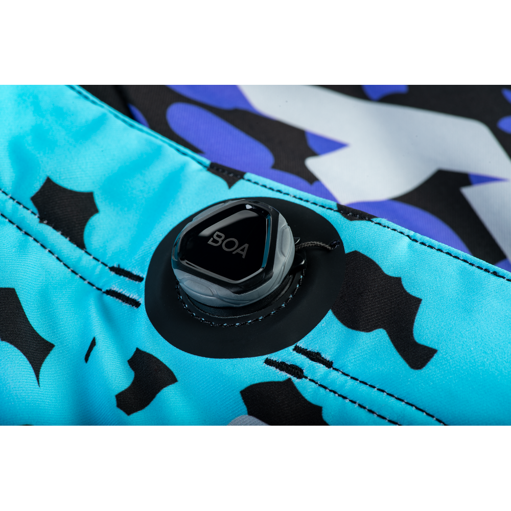 Close-up of a board shorts valve closure with a black BOA dial, set against a bright turquoise blue fabric with a black and white abstract pattern.