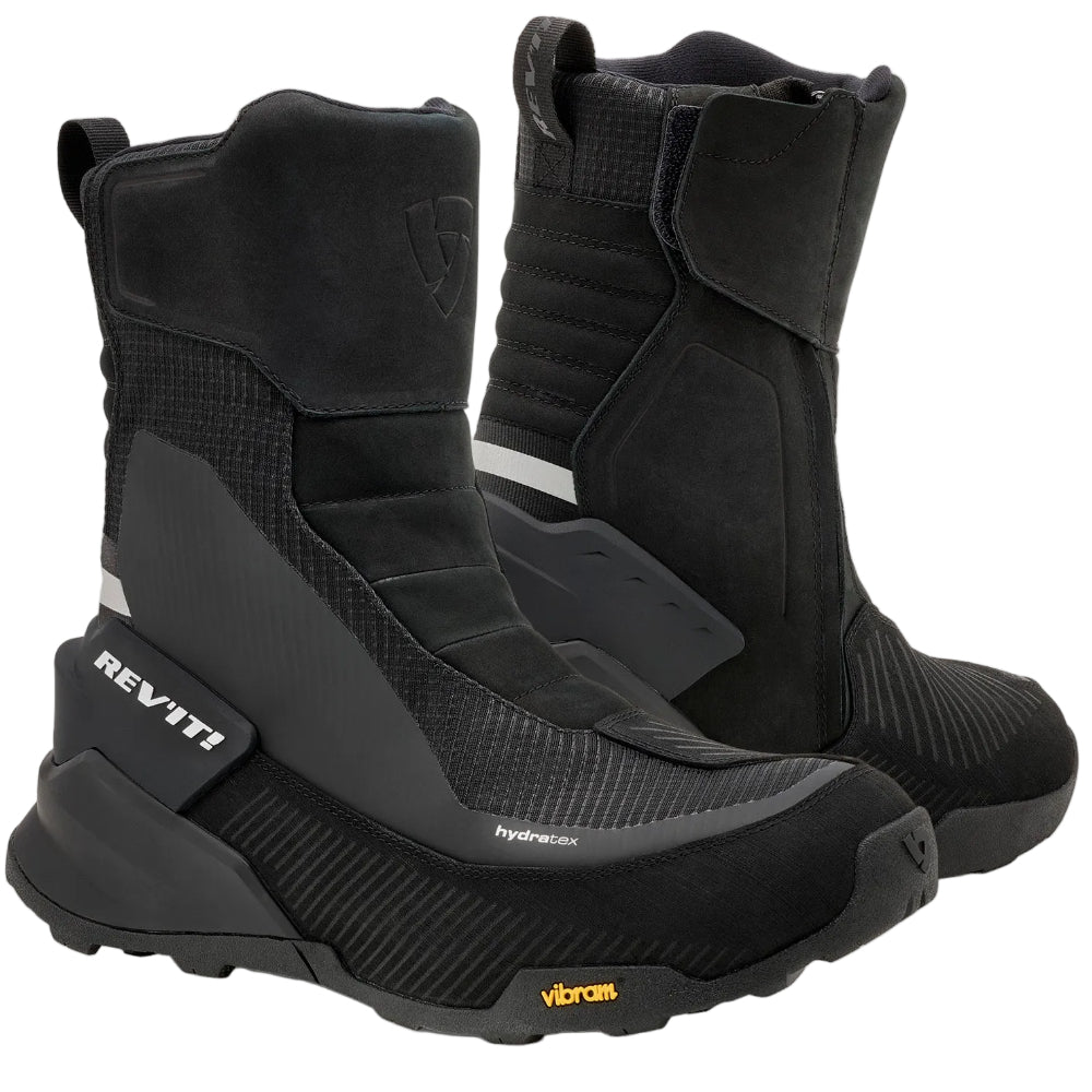 A pair of black REV'IT! mid-calf boots with textured panels and a small yellow Vibram logo on the toe, displayed against a light off-white background.