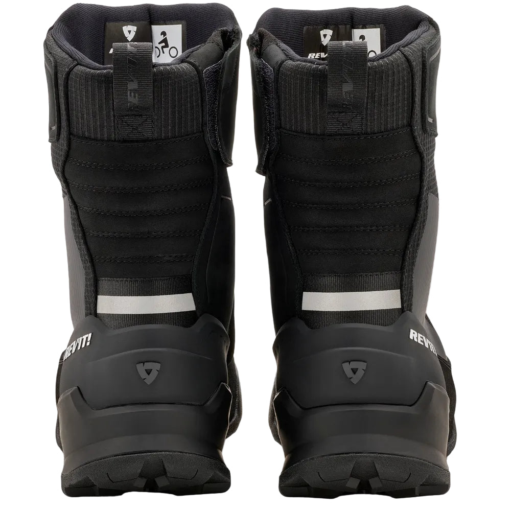 A pair of black motorcycle boots shown from the back, featuring textured black panels, a silver reflective stripe, and a black sole, set against a plain light gray background.