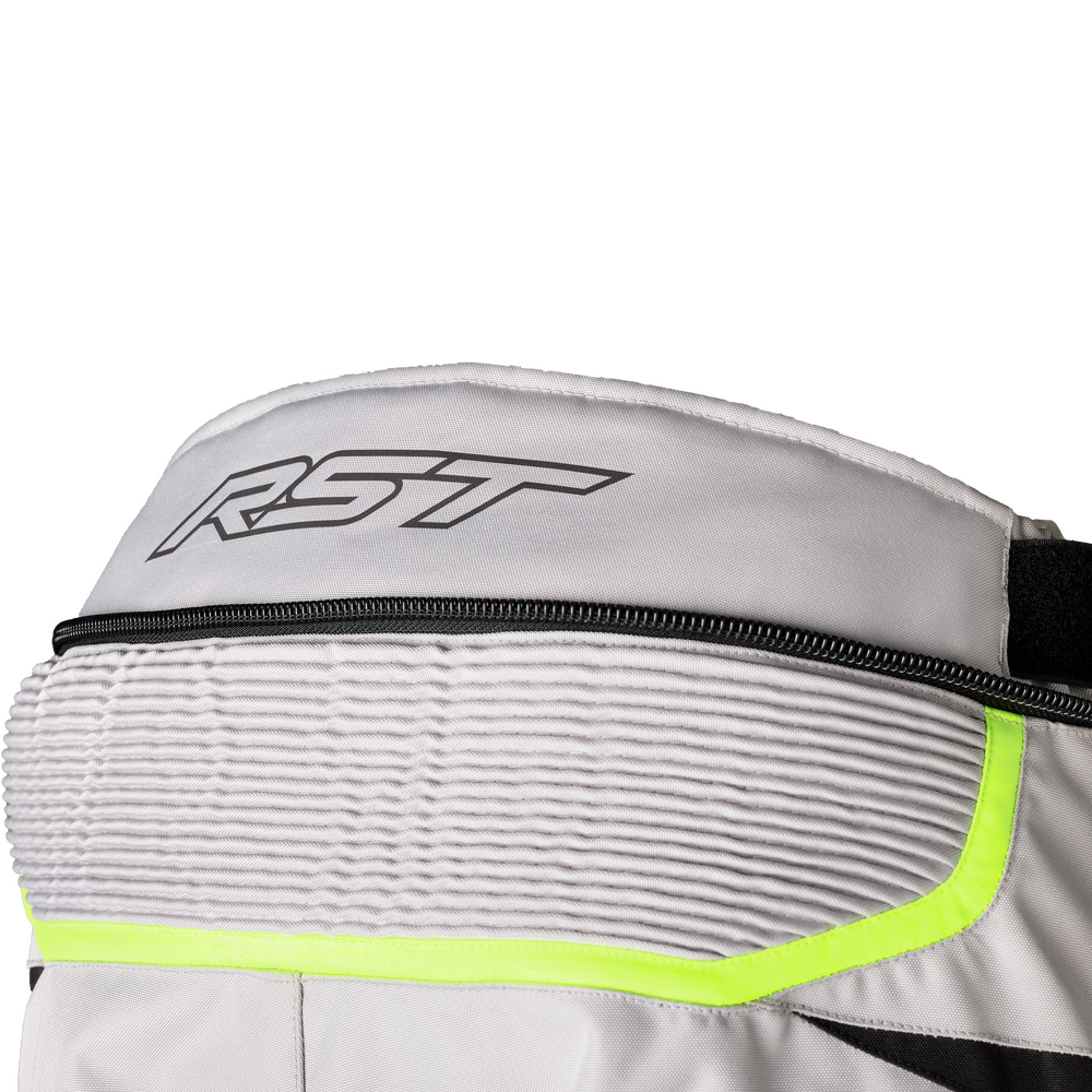 Close-up of a white and gray technical riding jacket or vest with a black zipper, a black outlined RST logo on the shoulder, and a bright neon yellow-green trim accent.