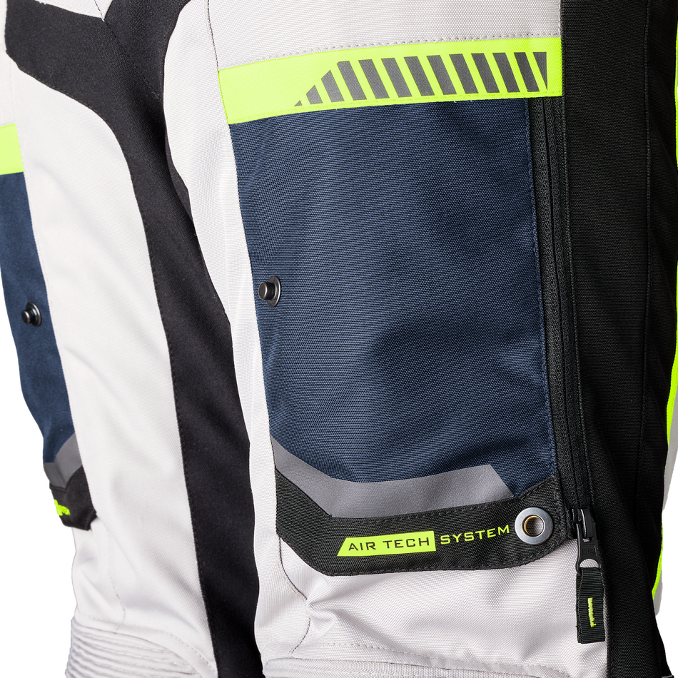 Close-up of a motorcycle jacket showing the side pocket with a black zipper, a black fabric tab labeled 'AIR TECH SYSTEM', and neon yellow-green reflective accents on a white, black, and navy panel layout.