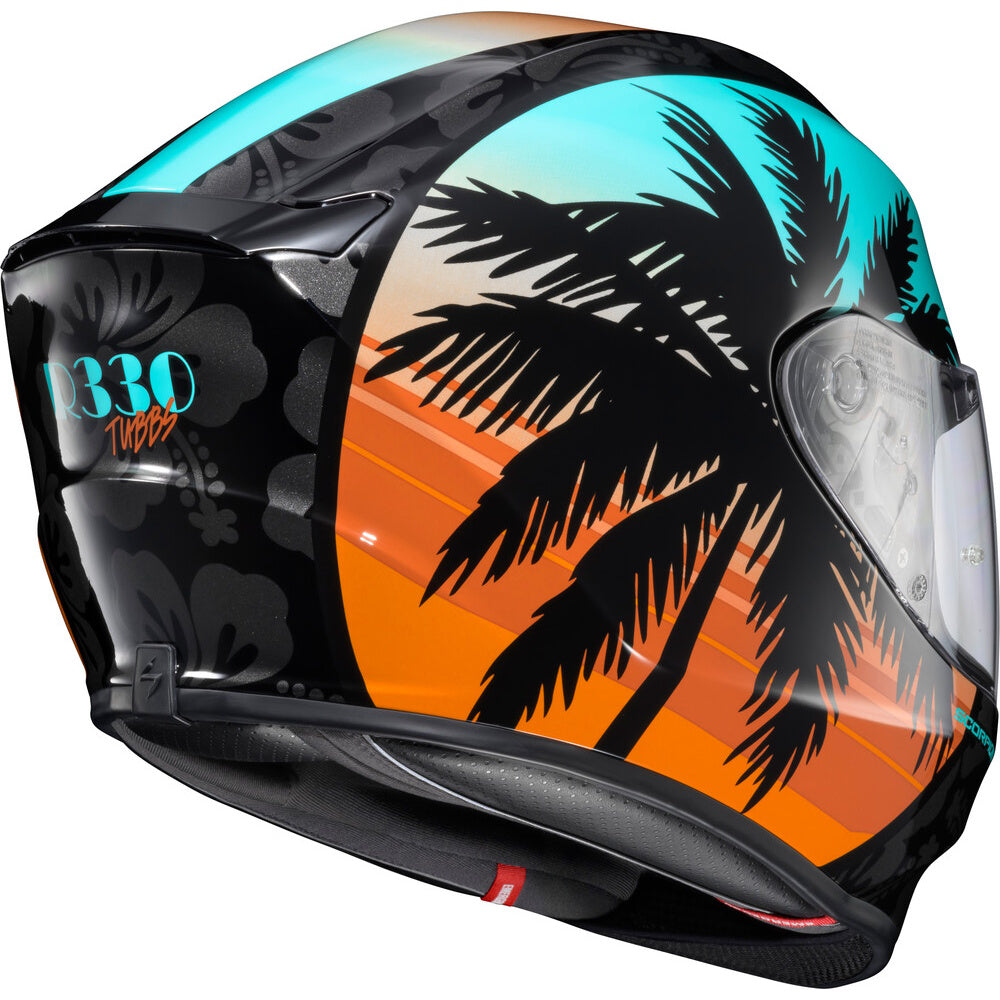 A full-face motorcycle helmet with a tropical sunset design, featuring black palm tree silhouettes over a gradient of orange, yellow, and turquoise blue, with a black floral pattern on the side.