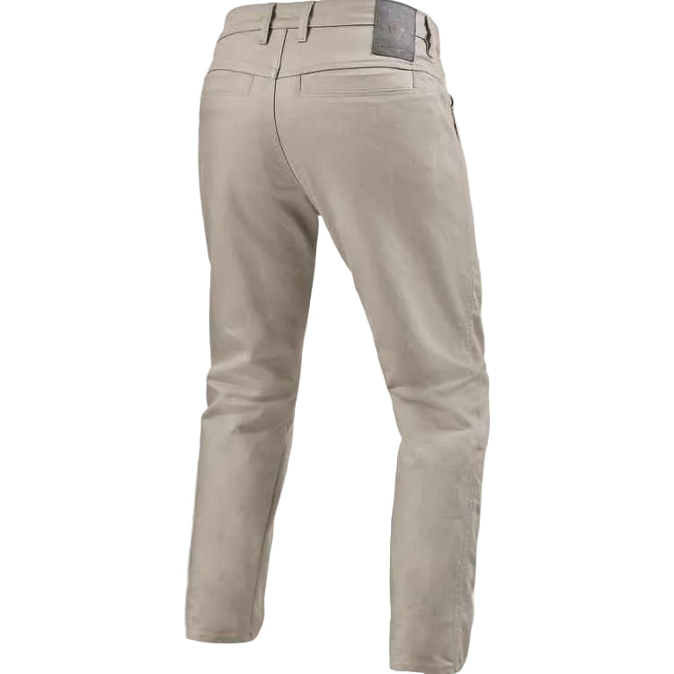 A pair of men's slim-fit trousers shown from the back, in a light taupe-beige color. The back waistband features belt loops, a button closure, and a small dark brand patch near the top right.