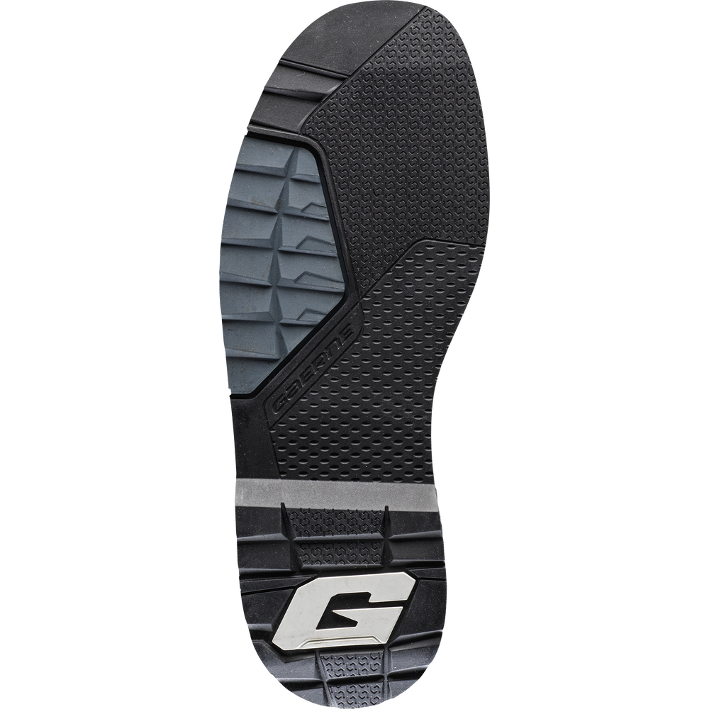The outsole of a shoe, featuring a black and dark gray tread pattern with a silver and black 'G' logo at the heel, on a solid white background.