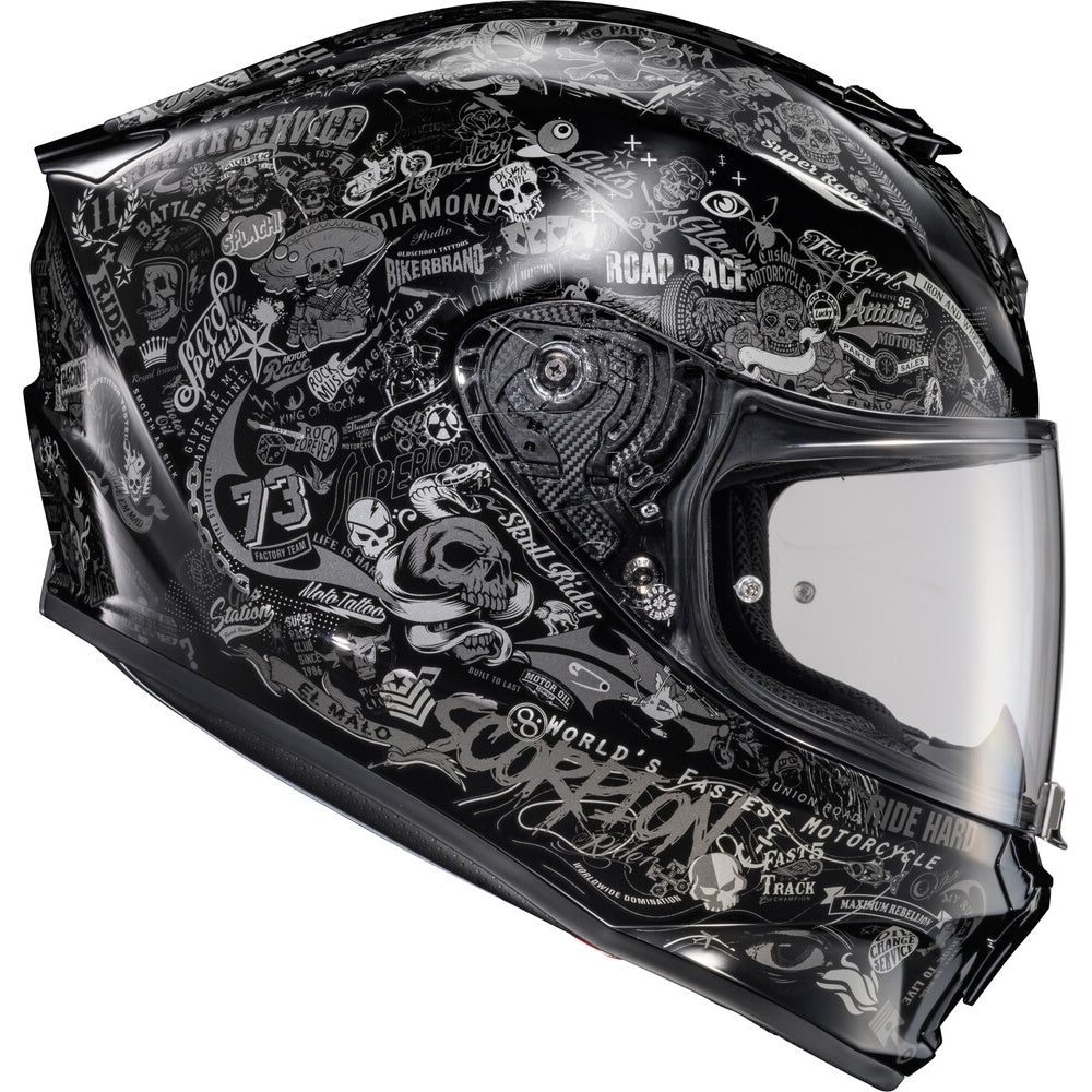A black full-face motorcycle helmet with an all-over white and gray graphic print featuring skulls, biker logos, and text such as 'Scorpion' and 'Road Race'. The helmet has a clear visor and is photographed on a solid white background.