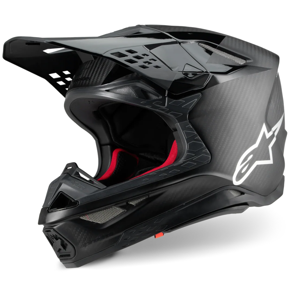 A black Alpinestars full-face motocross helmet with a carbon fiber pattern, featuring a white star logo on the side and red interior padding, shown on a white background.