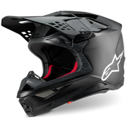 A black Alpinestars full-face motocross helmet with a carbon fiber pattern, featuring a white star logo on the side and red interior padding, shown on a white background.