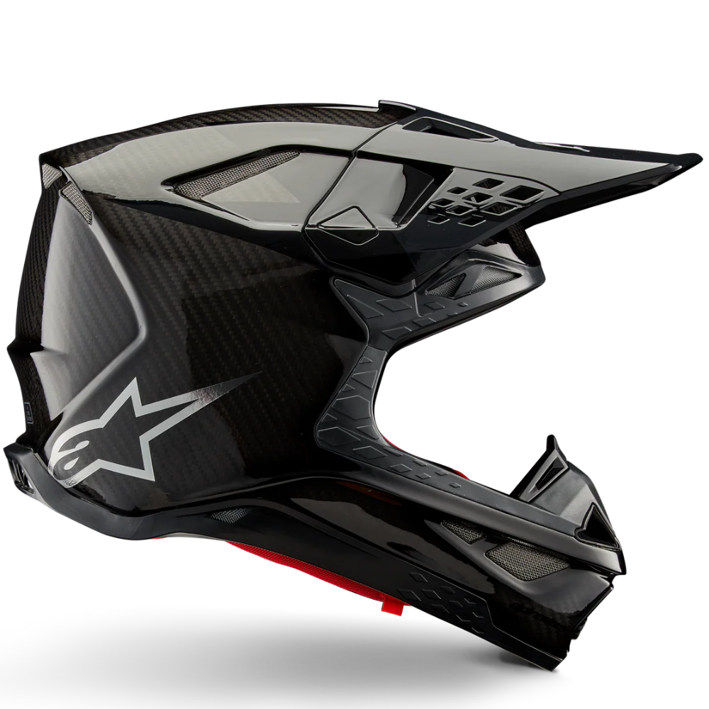 A black Alpinestars full-face motocross helmet with a carbon fiber pattern, featuring a white star logo on the side and a small red accent on the chin, shown against a white background with a soft shadow.