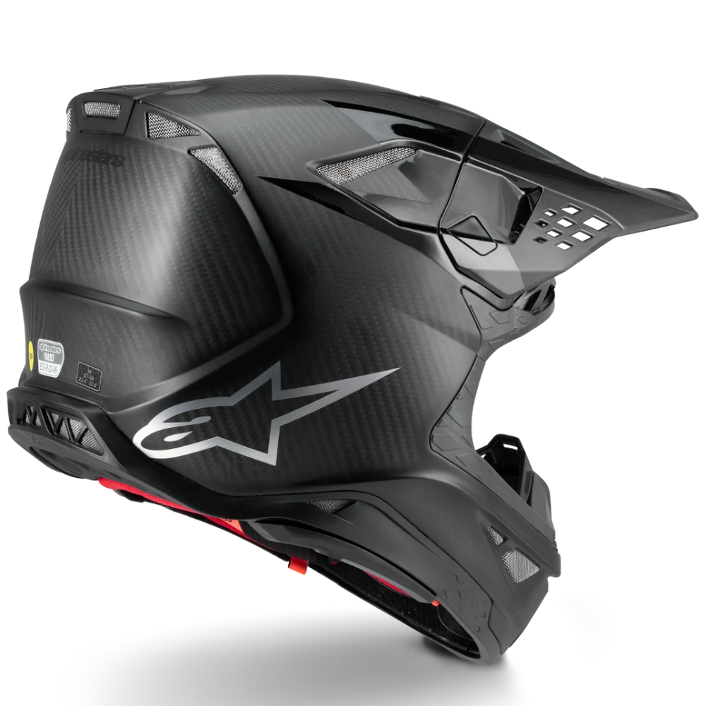 Alpinestars off-road motorcycle helmet in matte black with a carbon fiber pattern, featuring a silver Alpinestars logo on the side and a small red accent near the chin.