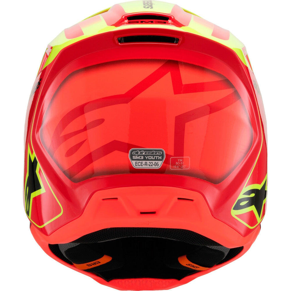 A close-up rear view of a red Alpinestars full-face motocross helmet with neon yellow and black graphic accents, featuring a clear visor and a visible ECE-122.02 certification sticker.