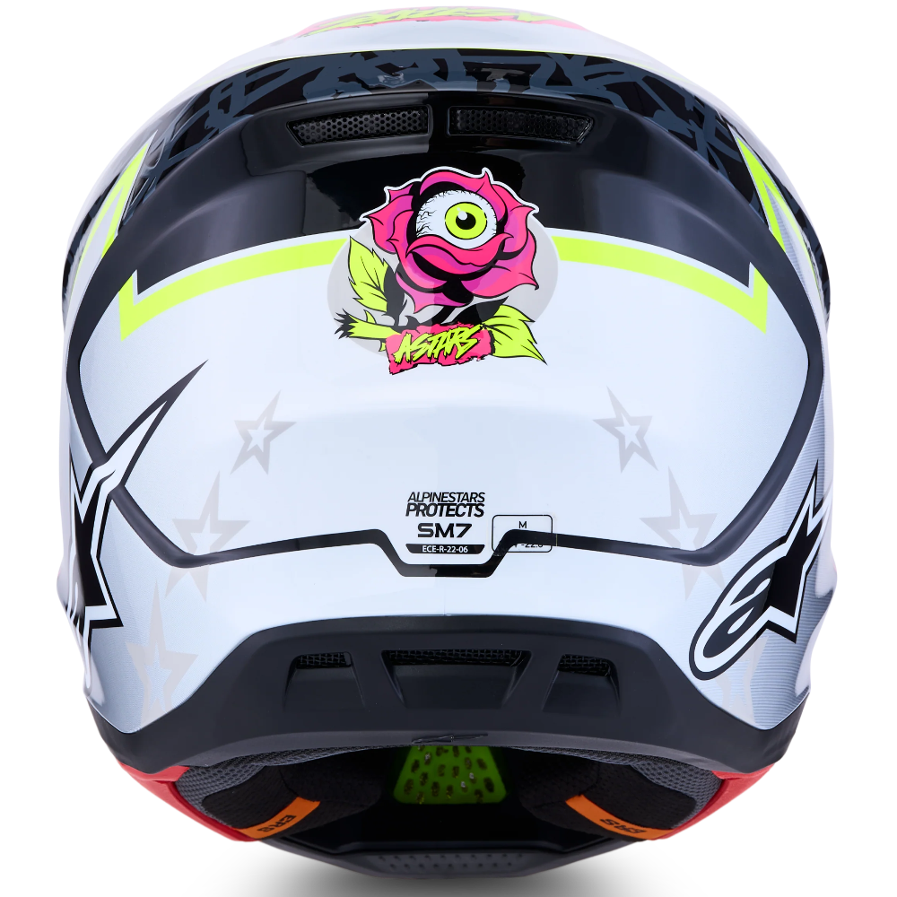 A white Alpinestars full-face motocross helmet with black graphics, lime green accents, and a pink cartoon monster sticker on the visor, shown against a white background.