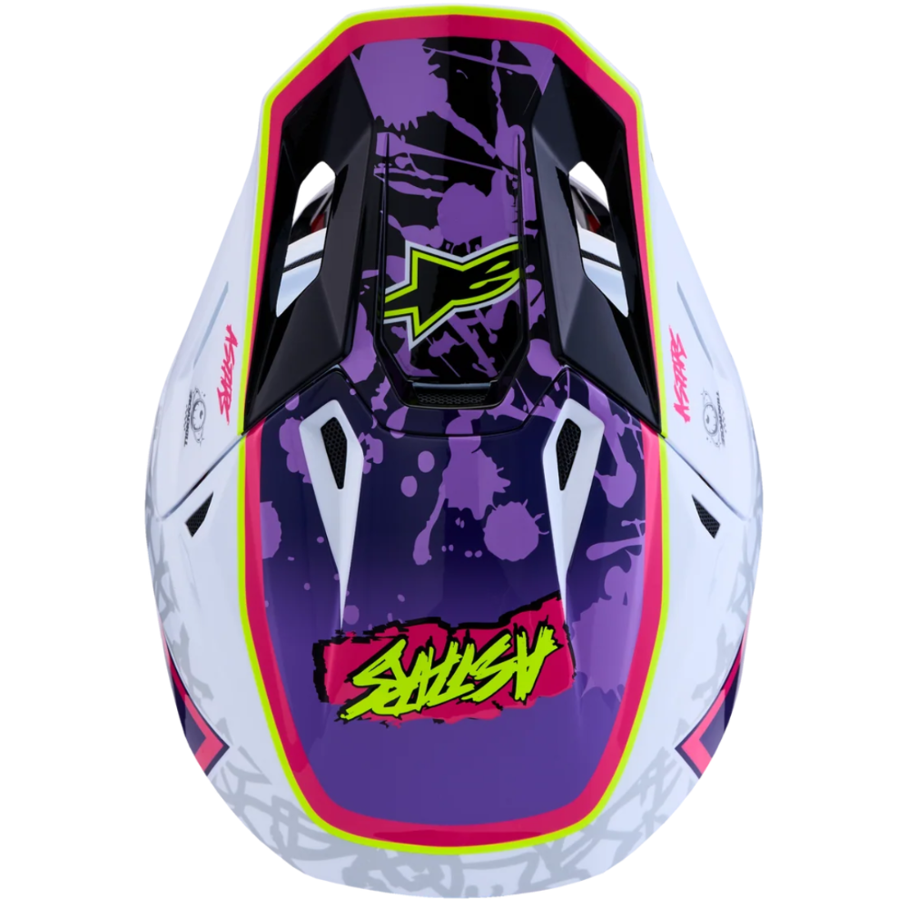 Front view of a motocross helmet with a purple splatter graphic, neon pink and yellow accents, and a stylized 'SHUSHY' logo on a white background.
