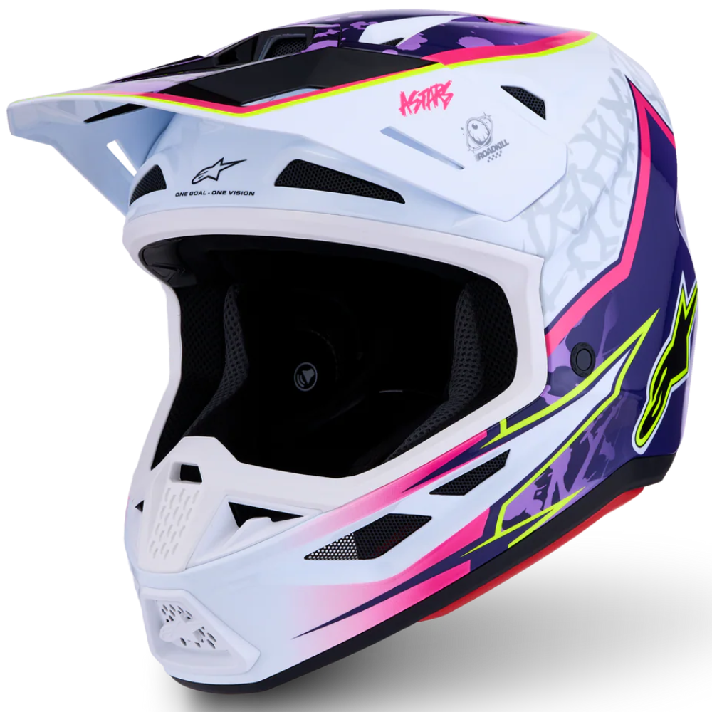 A white Alpinestars motocross helmet with vibrant pink, purple, and neon green graphic accents, shown from a three-quarters angle on a white background.