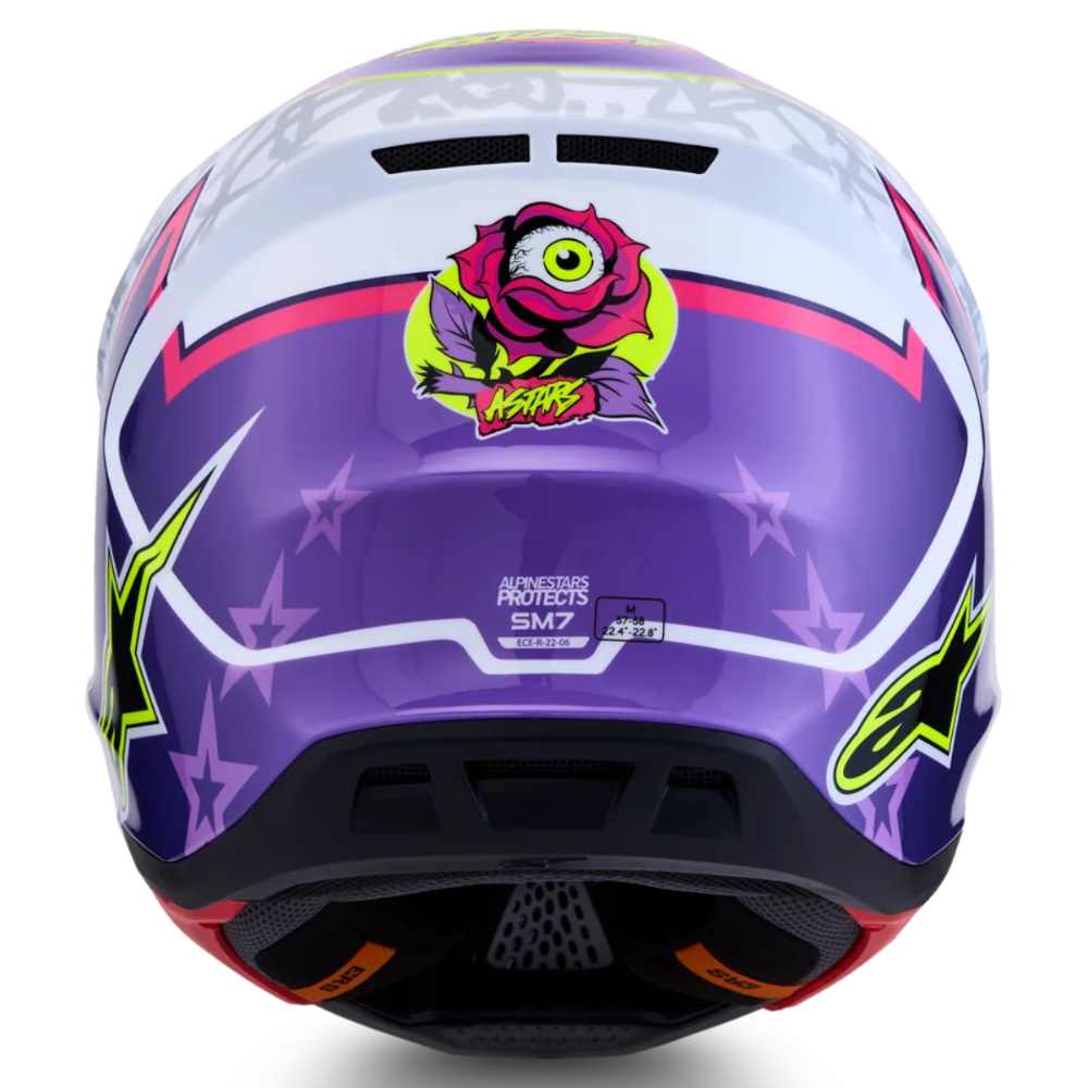 A full-face motocross helmet shown from the rear, featuring a purple and white graphic design with pink and green accents, including a cartoon monster sticker and Alpinestars branding.