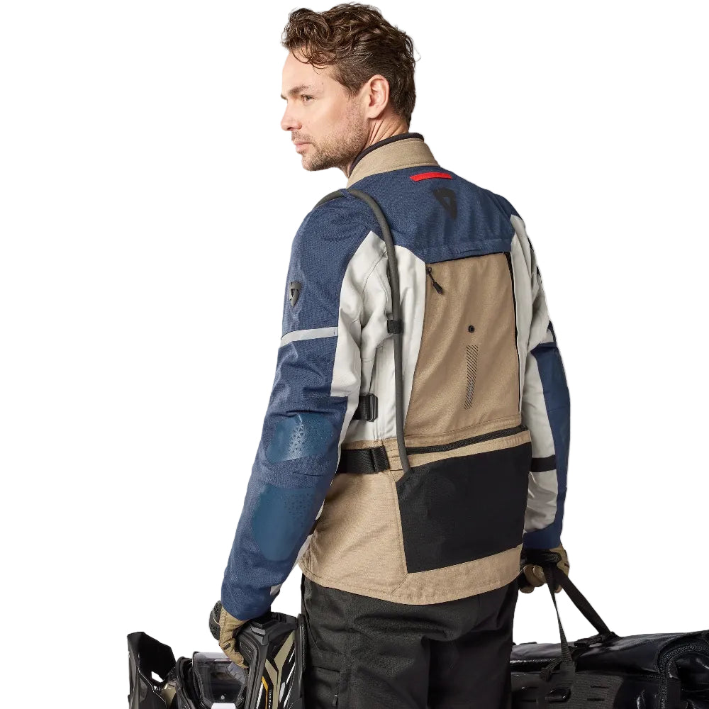 Man wearing a multi-colored jacket with a backpack, standing against a white background