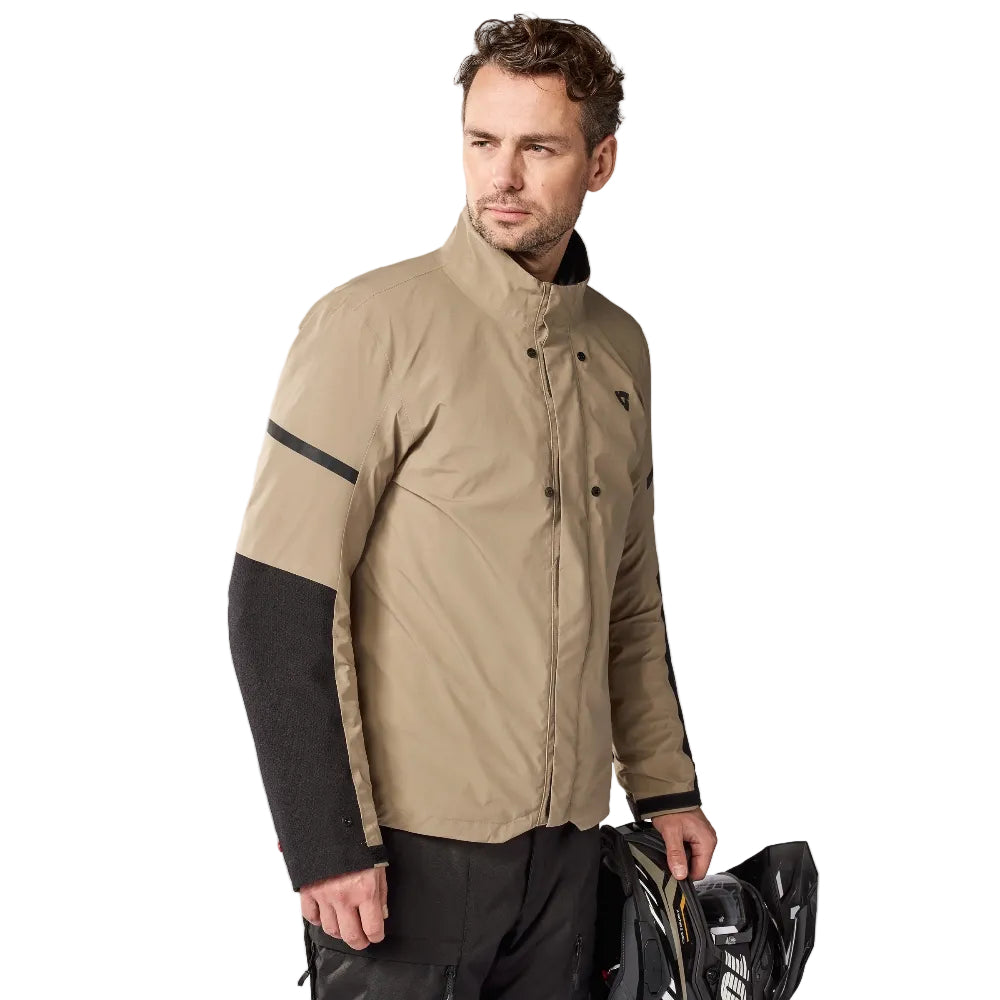Man wearing a beige and black jacket holding a helmet on a white background