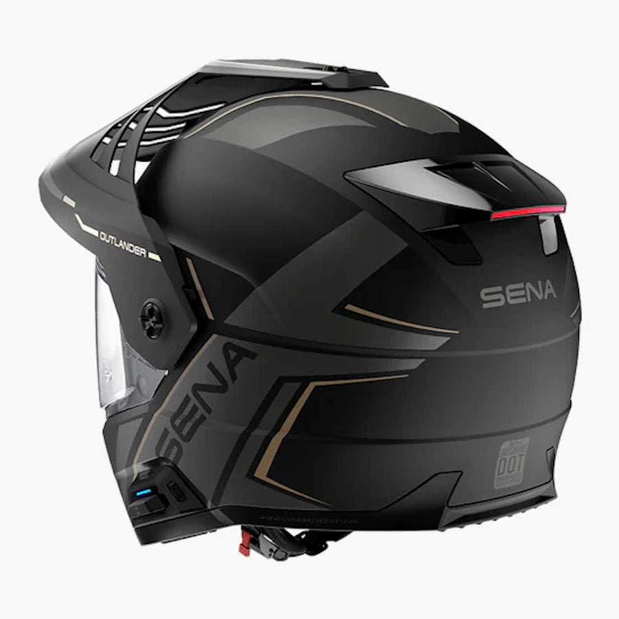 A matte black full-face motorcycle helmet with gold geometric accents and a clear visor, shown from a three-quarters angle on a light gray background. The brand 'SENA' is clearly visible on the side and rear of the helmet.