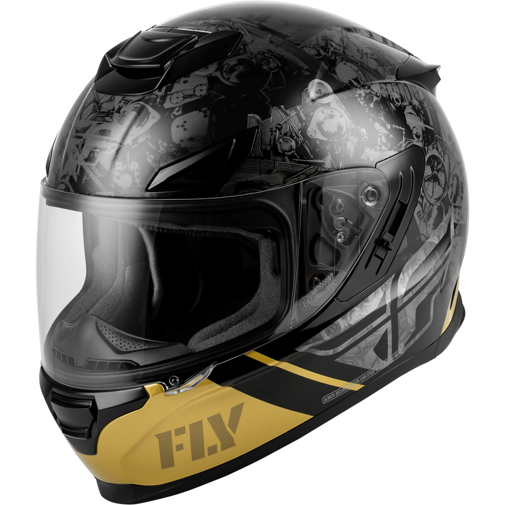 A full-face motorcycle helmet with a glossy black base, gray graphic patterns across the shell, and a prominent gold chin bar featuring the 'FLY' brand logo. The helmet is shown at a three-quarter angle against a plain white background.